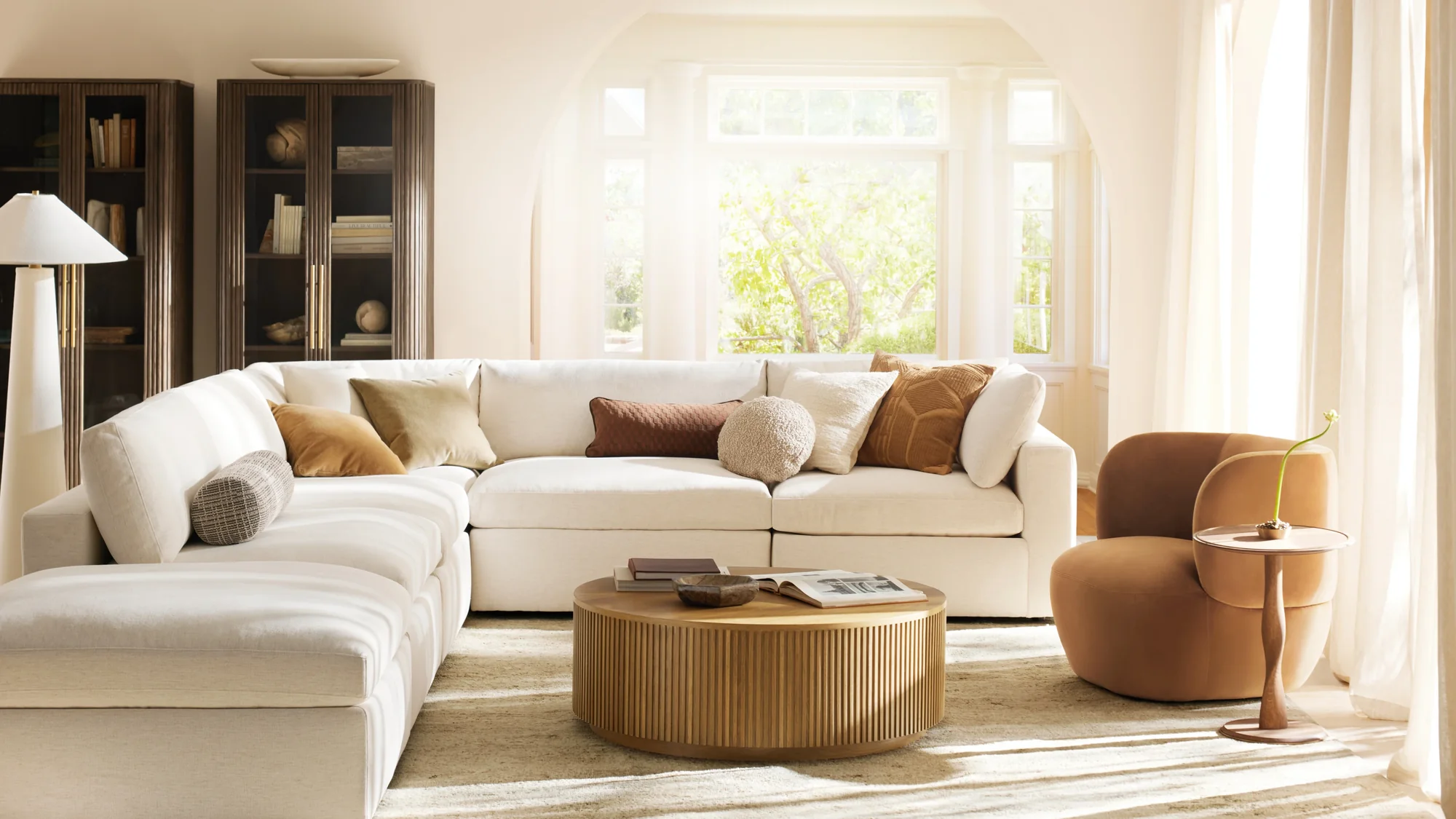 Bright living room with a white sectional sofa, wooden coffee table, brown armchair, and tall bookshelves.