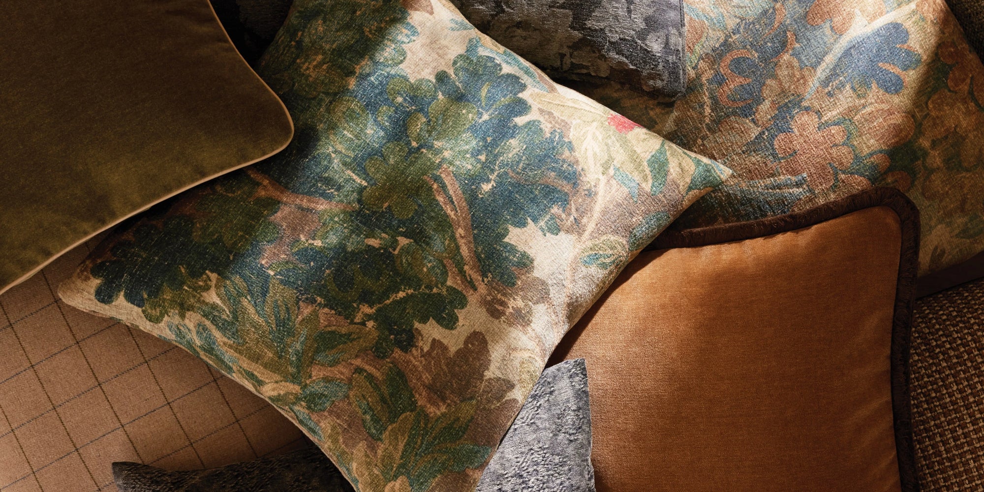 A cozy grouping of pillows in a mix of textures, from soft velvet to woven fabrics, displayed in a rich fall color palette of warm rust, deep gold, earthy brown, and muted olive. The layered tones and materials create an inviting, seasonal look perfect for autumn décor.