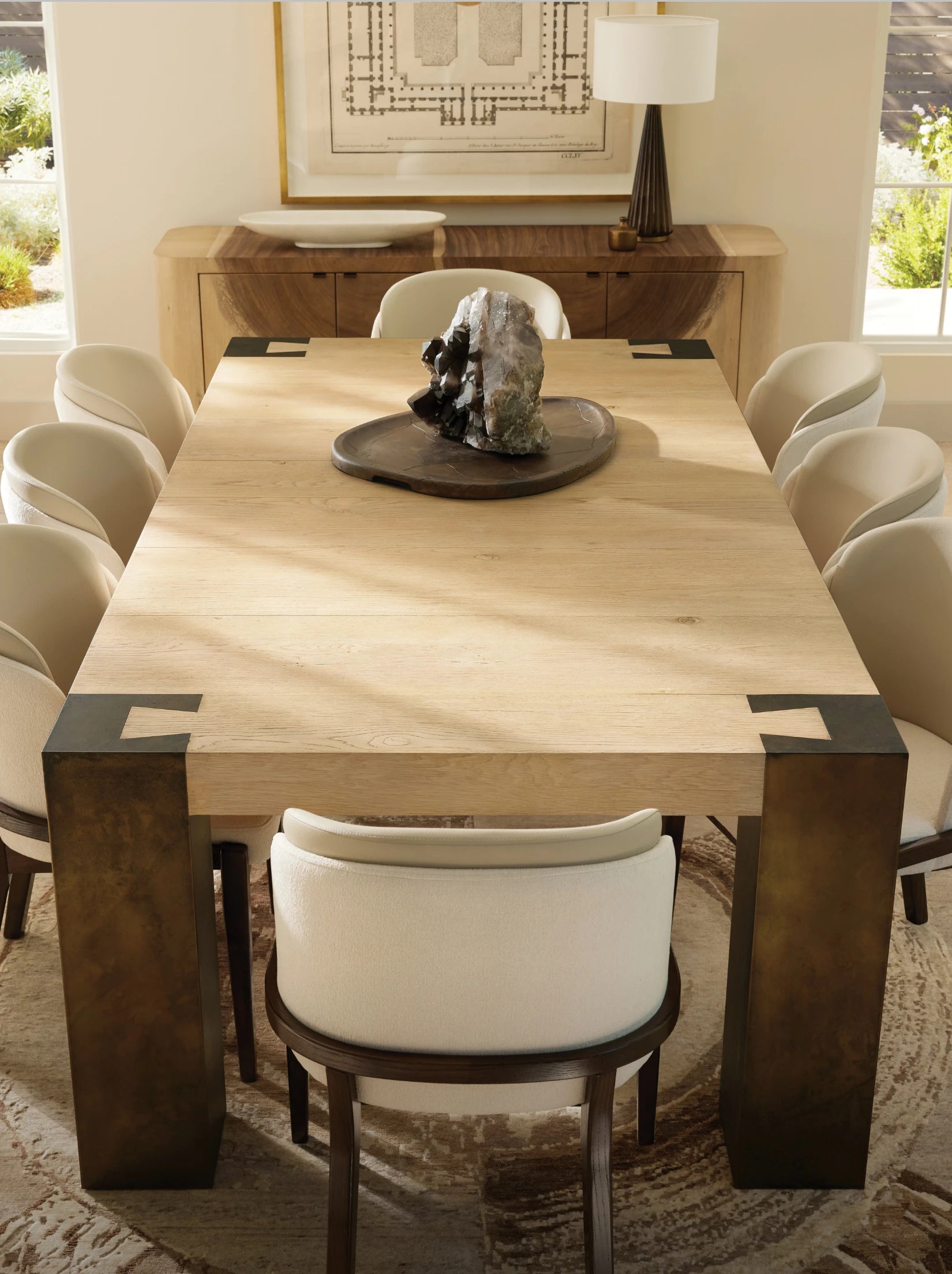 Dining room with light wood table, cream chairs, stone centerpiece, and framed artwork on wall.