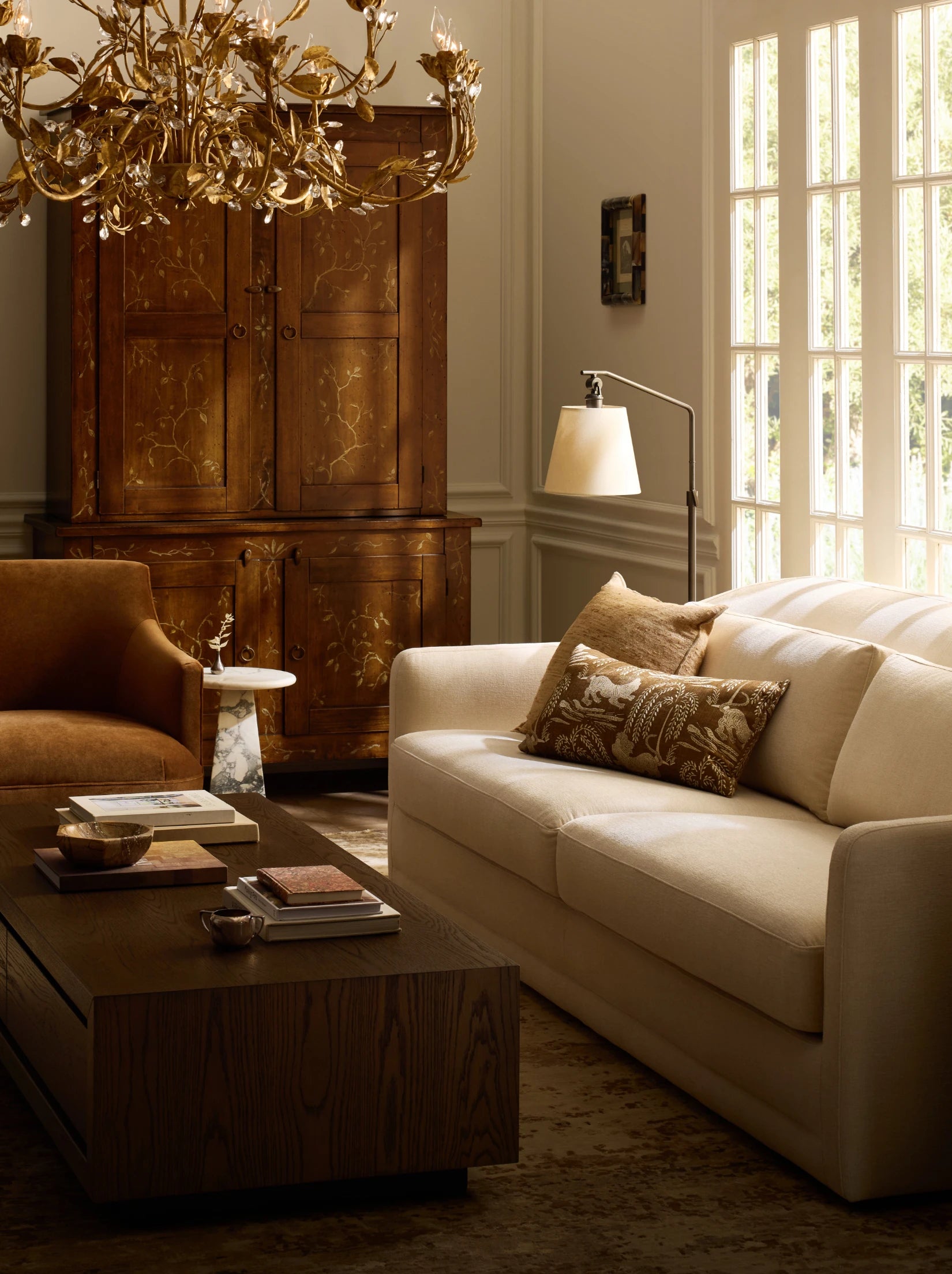 Living room with cream sofa, brown armchair, wooden coffee table, and ornate gold chandelier.