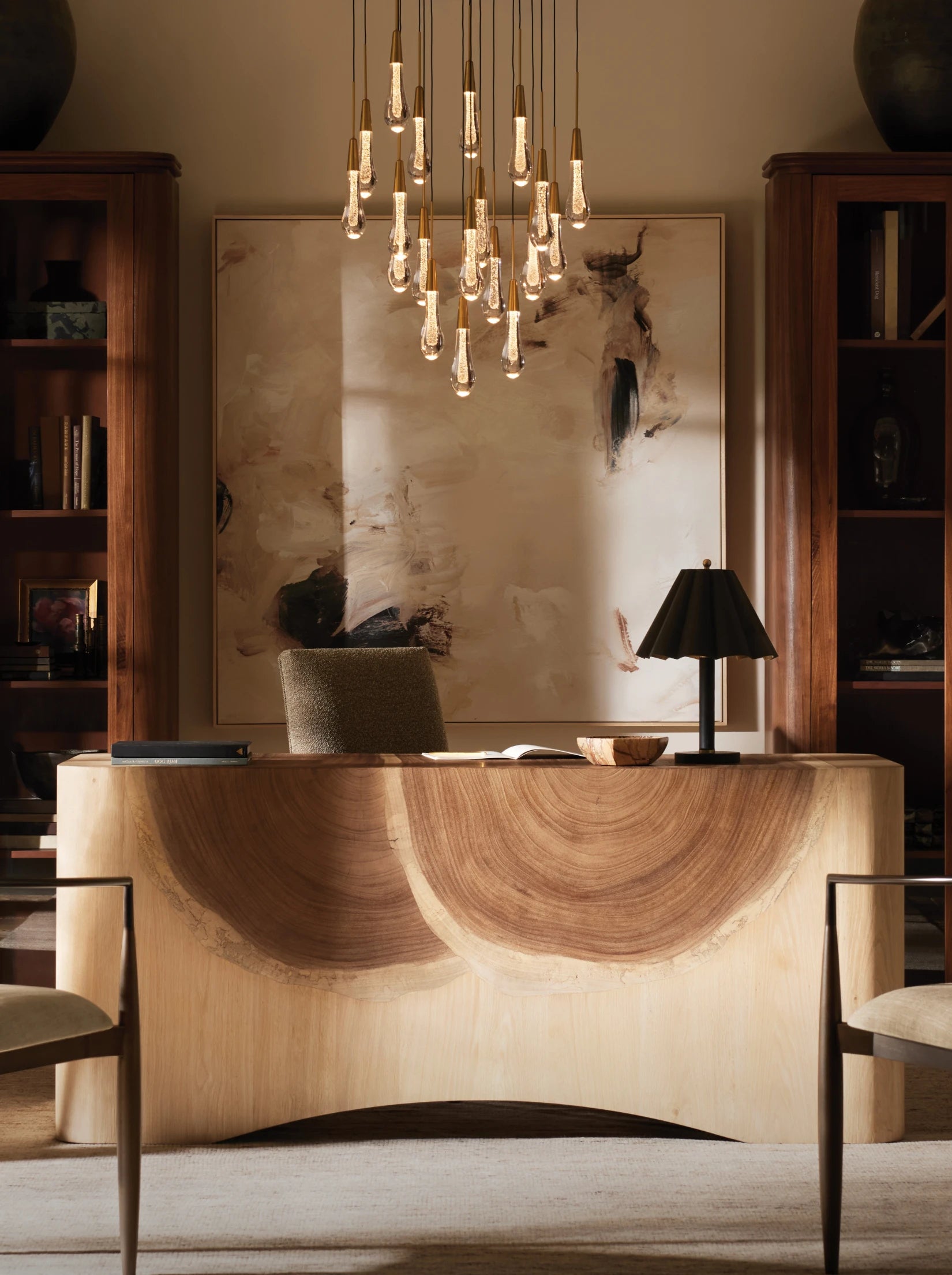 Office with curved wooden desk, abstract wall art, pendant lights, and built-in bookshelves.