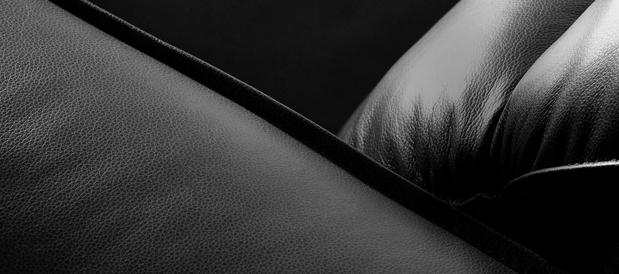 Close-up of rich black leather upholstery, showing its natural grain and soft creases in dramatic, low-angle lighting.