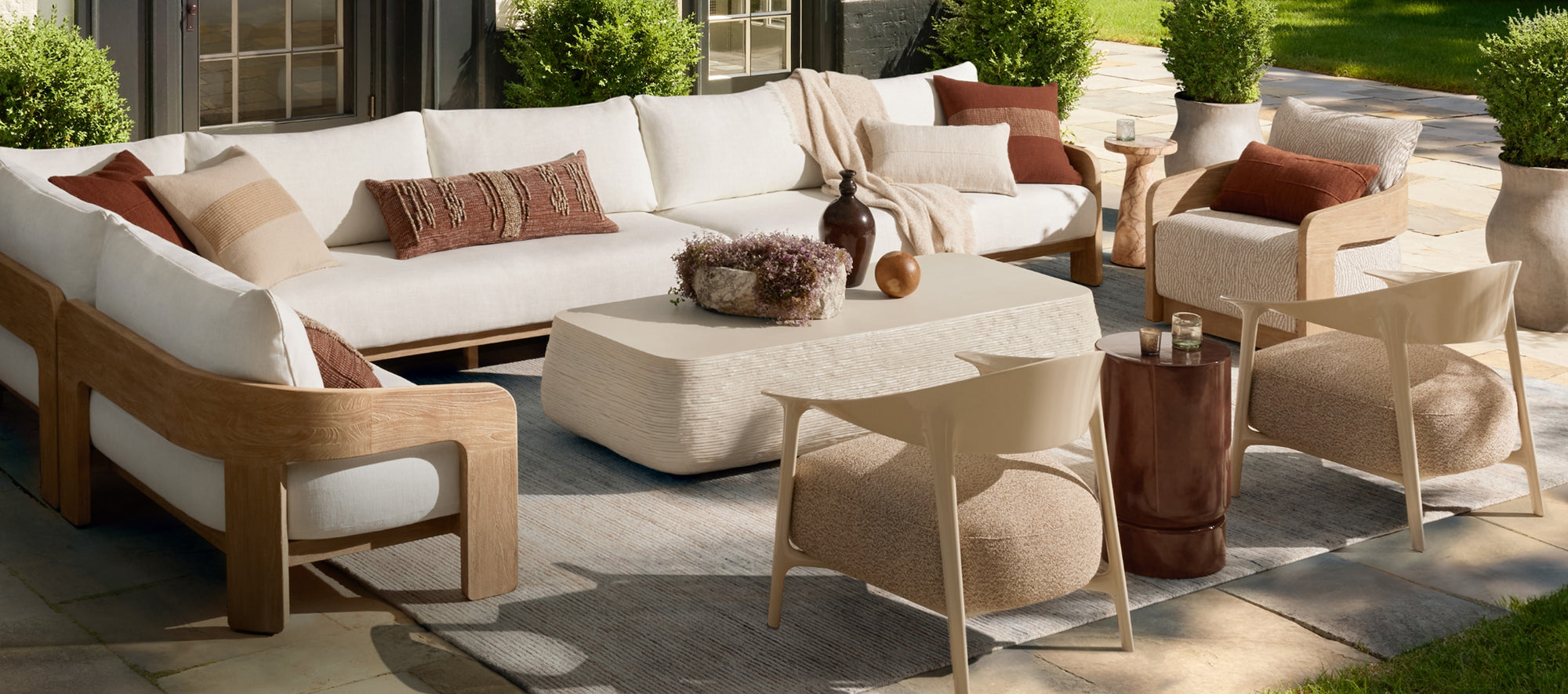 Expansive outdoor living space featuring cushioned seating, warm wood tones, and layered textiles, set in a bright, open-air environment.