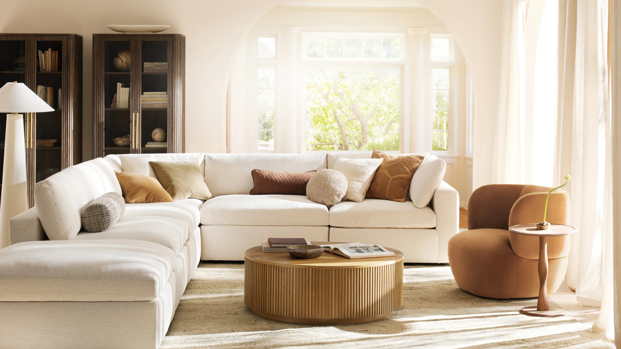 Bright living room with a white sectional sofa, wooden coffee table, brown armchair, and tall bookshelves.