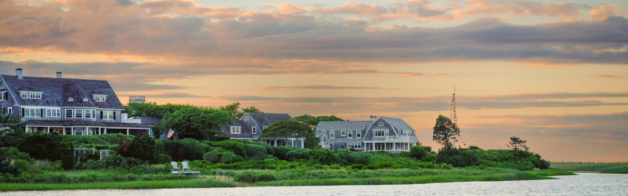Waterfront New England homes at sunset with elegant homes, lush gardens, and calm reflective water.