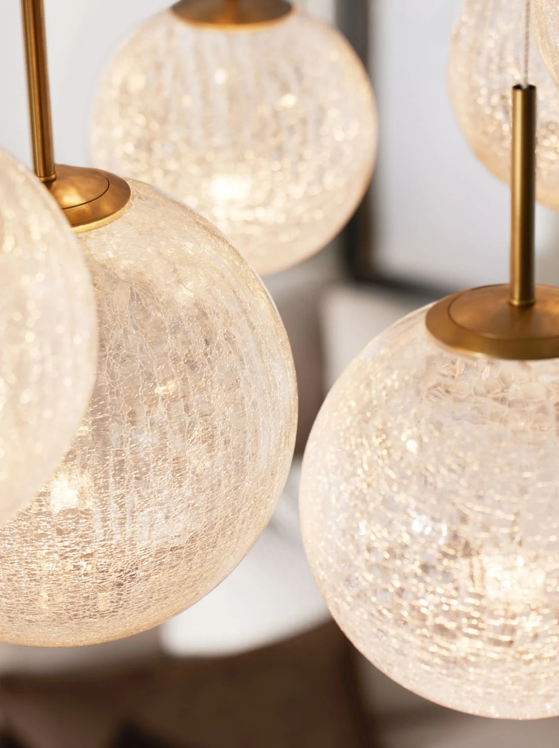 A close-up of globe pendant lights with textured, crackled glass and warm brass fittings. The softly glowing bulbs inside create a shimmering effect, highlighting the intricate glass pattern and casting a warm, ambient light.