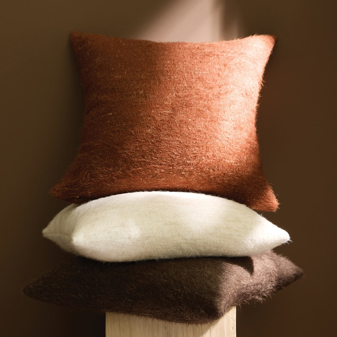 Stacked decorative accent pillows in warm earthy tones, showcasing soft textures and layered autumn-inspired styling.