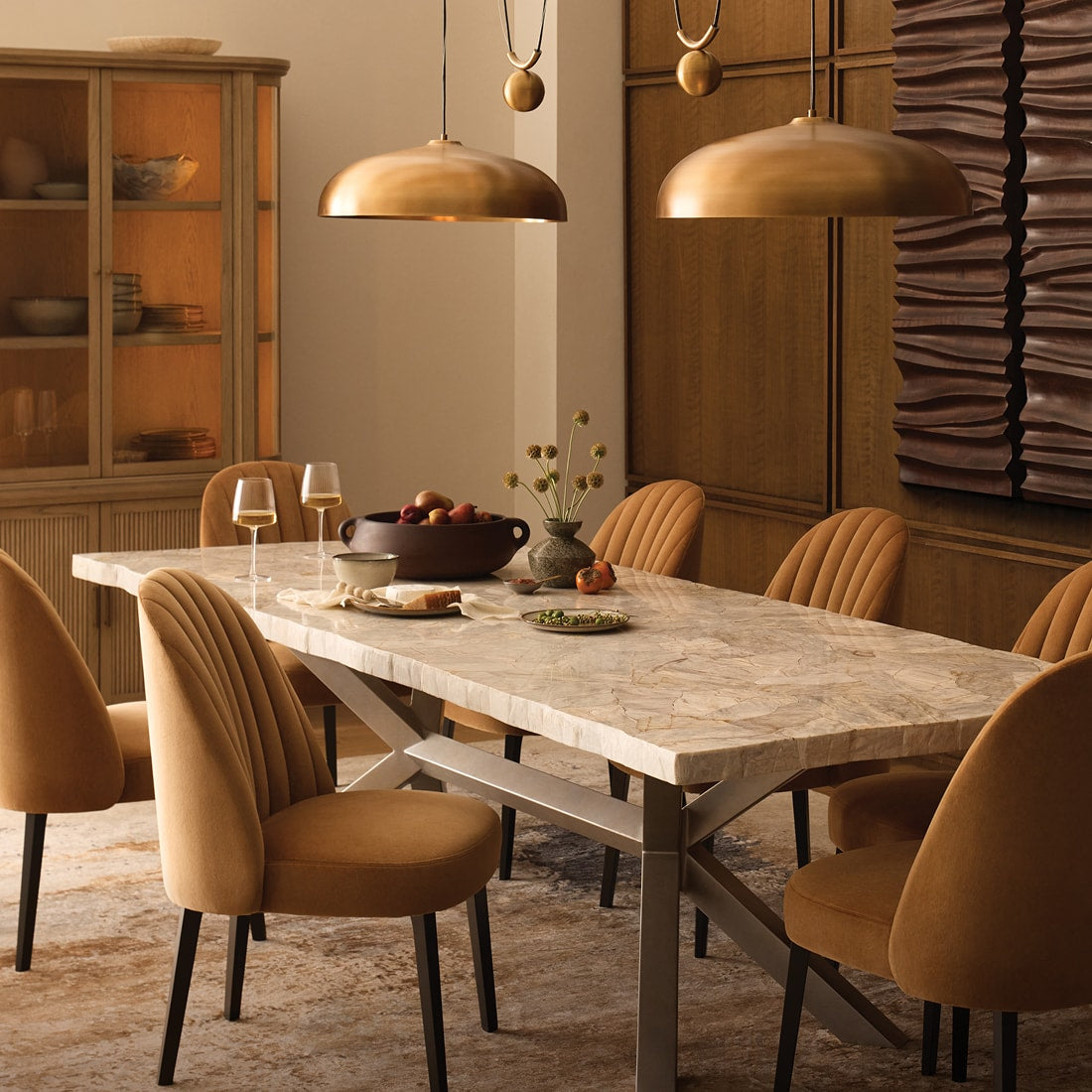 Dining room with a stone table, upholstered dining chairs, and warm metallic pendant lights, styled with seasonal tabletop accents.