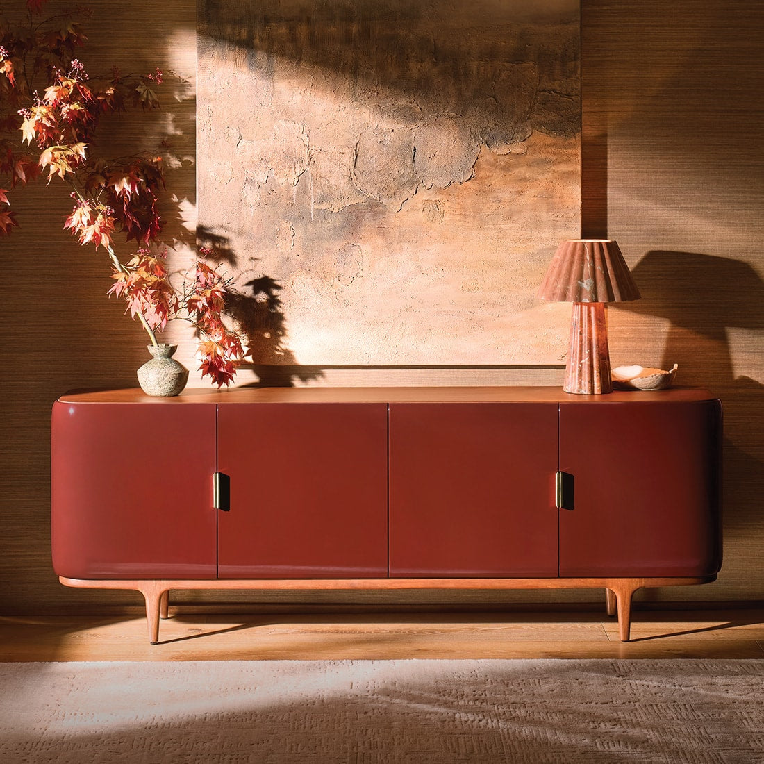 Curved lacquer sideboard styled with sculptural decor, autumn foliage, and layered artwork, creating a warm and inviting entryway vignette.
