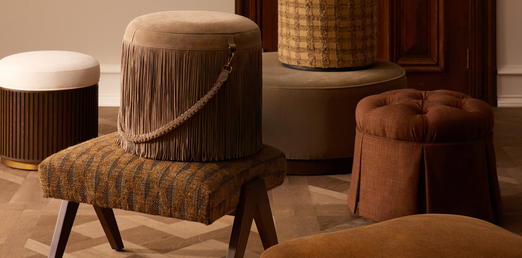 Collection of upholstered poufs and ottomans in warm neutral and earthy tones, showcasing varied textures, fringe detailing, and versatile accent seating.