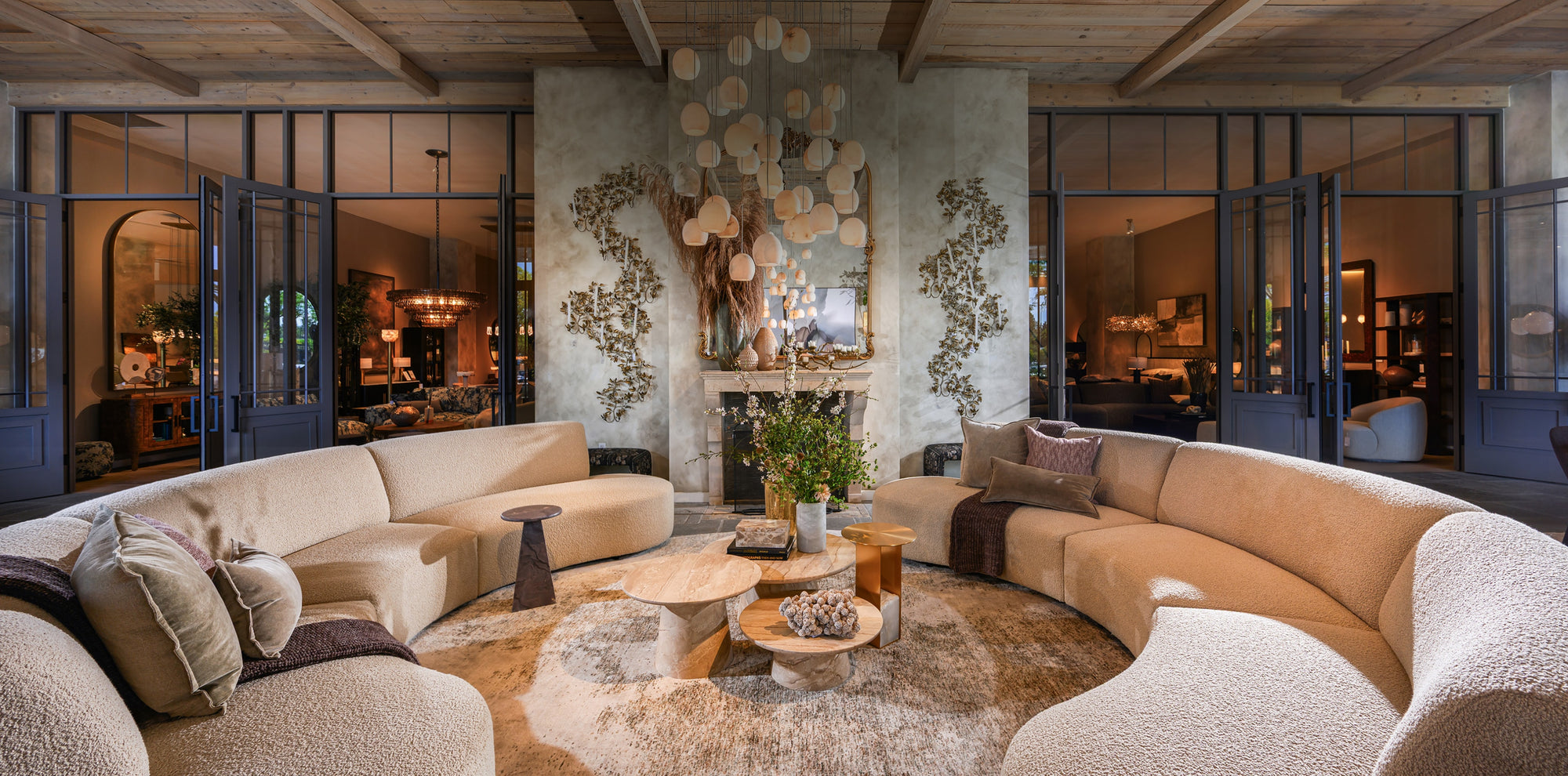 Expansive showroom featuring curved upholstered sofas, sculptural lighting, layered natural materials, and thoughtfully arranged furnishings in an elegant open-concept setting.