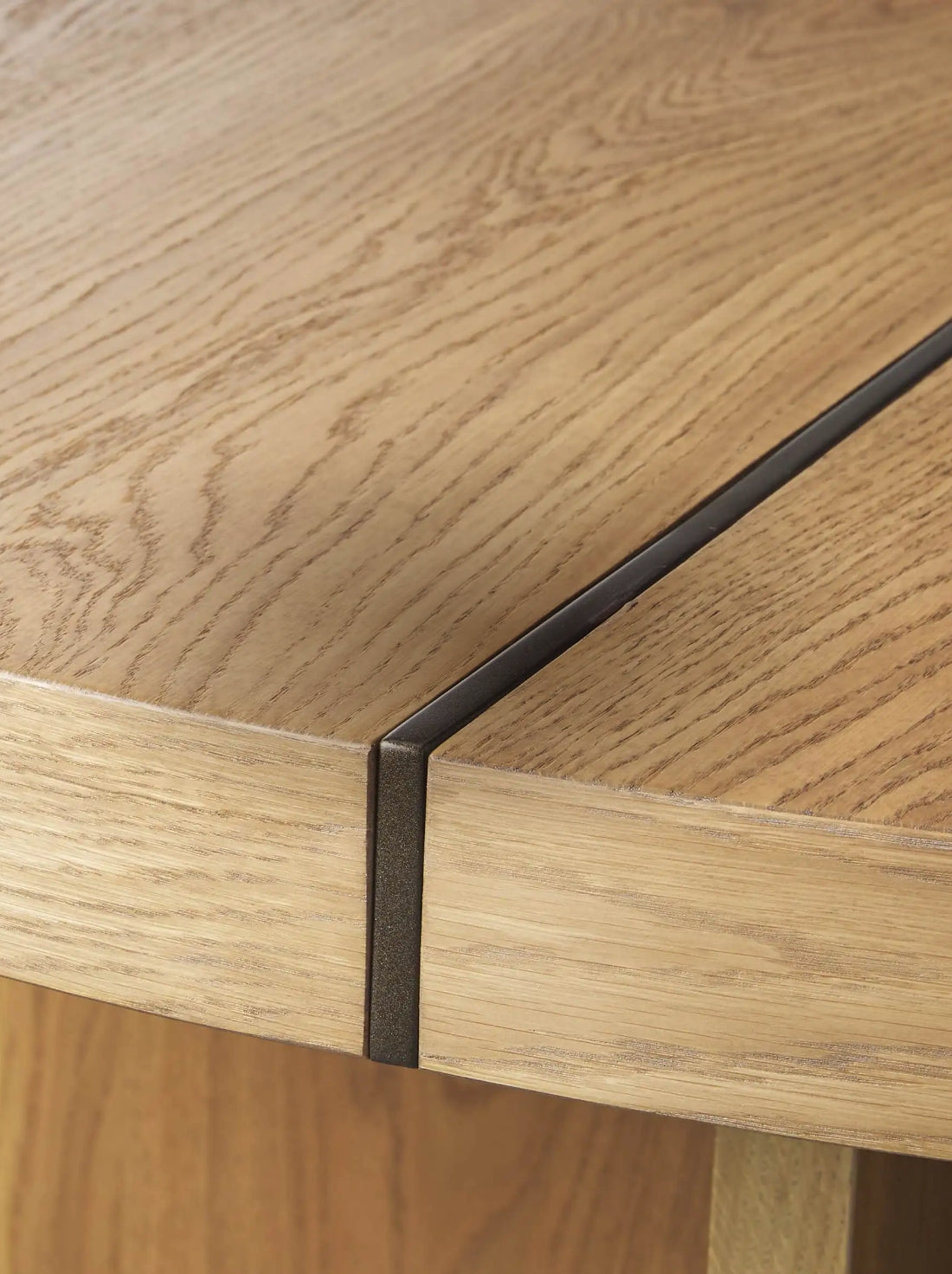Close-up of a wooden table edge with a warm, natural grain. A slight gap is visible, revealing a metal parting strip. The design feels modern and sleek.
