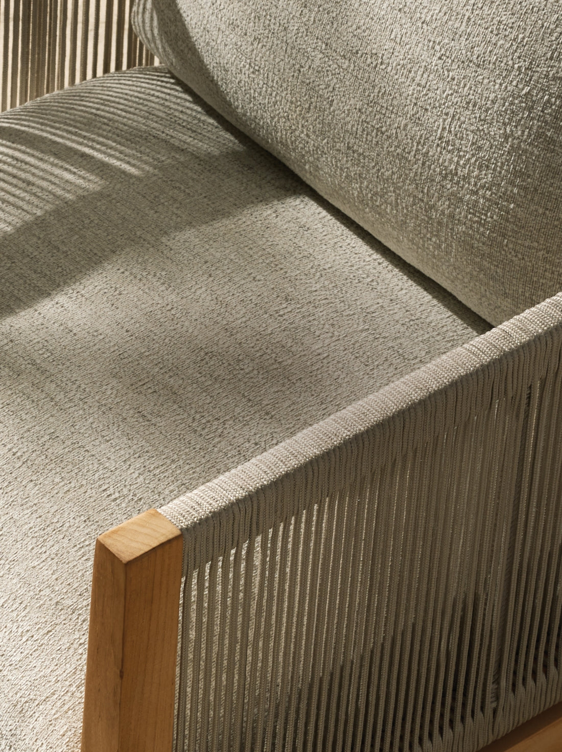 Close-up of a modern chair featuring a light gray textured cushion, wooden armrest, and vertical fabric ropes creating a sleek, minimalist design.