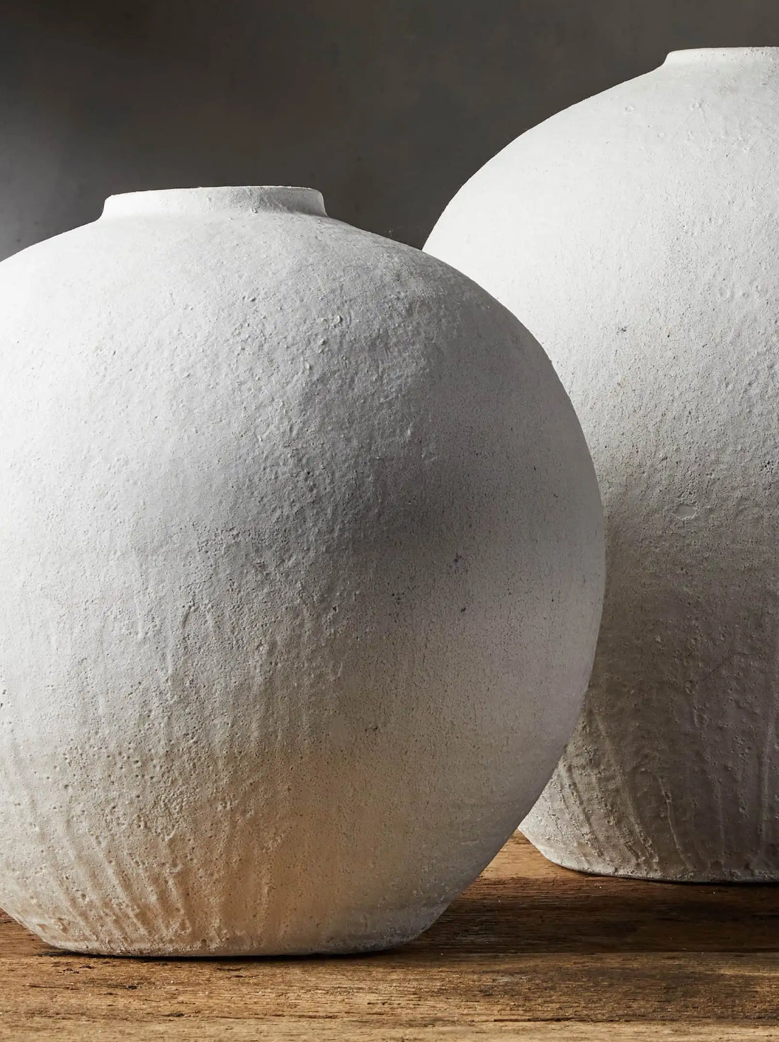 Two large, textured white clay vases on a wooden surface. The natural texture and earthy tones create a serene and minimalist atmosphere.