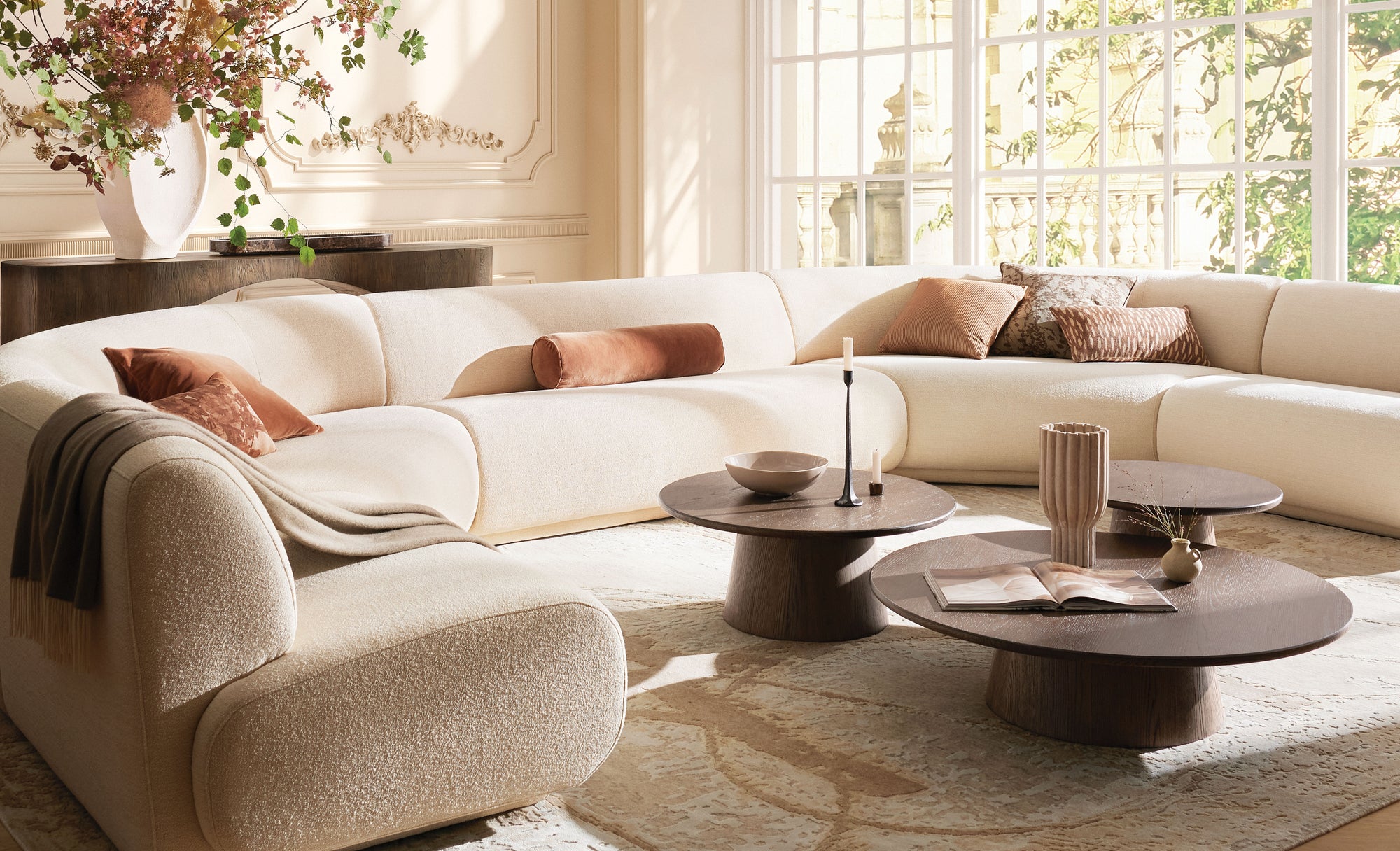 Modern living room with a white sectional sofa, wooden coffee tables, and decorative pillows.
