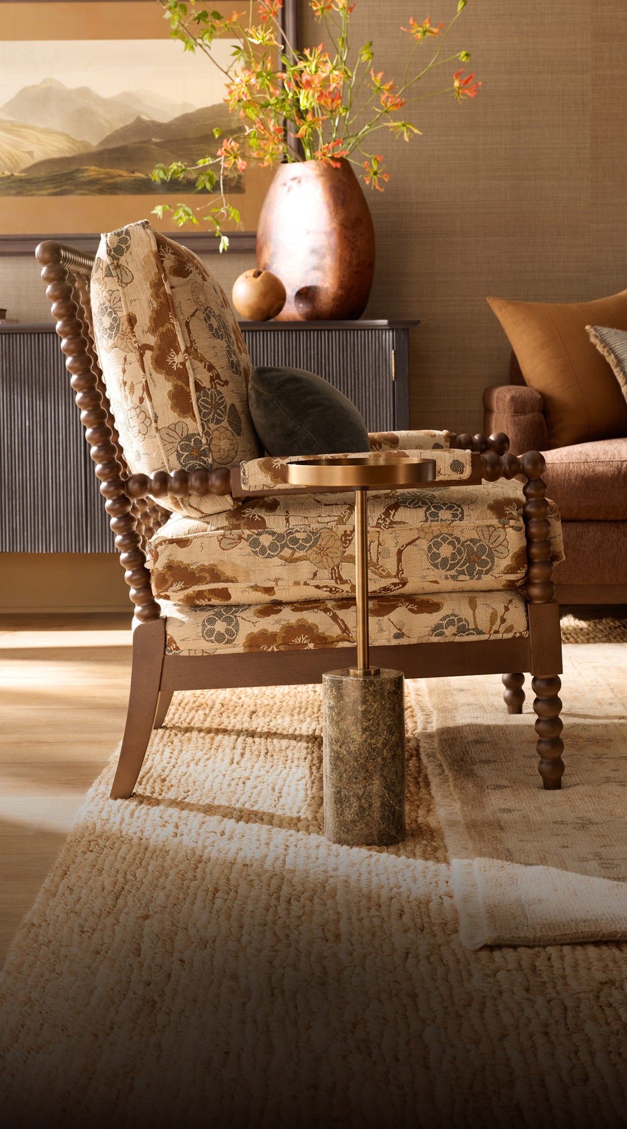 Traditional ccent chair with floral-patterned upholstery and turned wood detailing, styled with layered textiles, warm wood furnishings, and decorative accents in a richly textured living space.